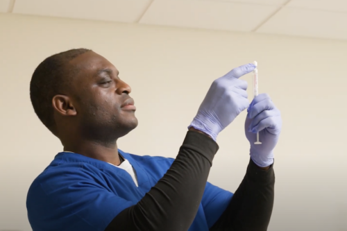 nursing student daniel in blue nursing scrubs looking at a syringe in his hand