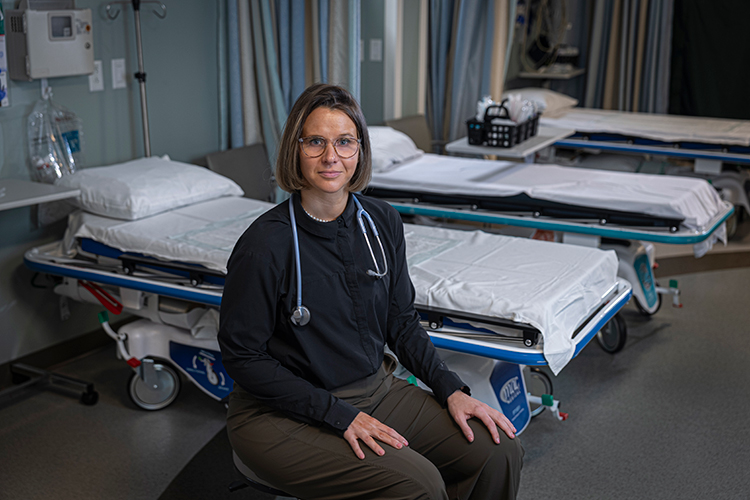 Laura sitting next to empty patient beds with a stethoscope around her neck, looking at the camera