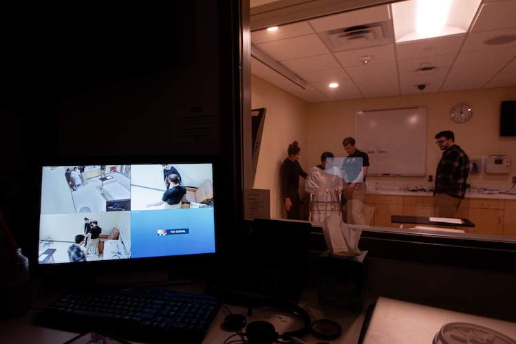 watching the patient and PT students through the simulation glass with the computer in the foreground showing cameras of the ICU