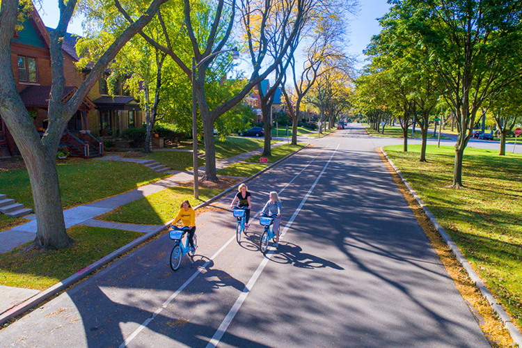 Three students riding bikes down boulevard on sunny day