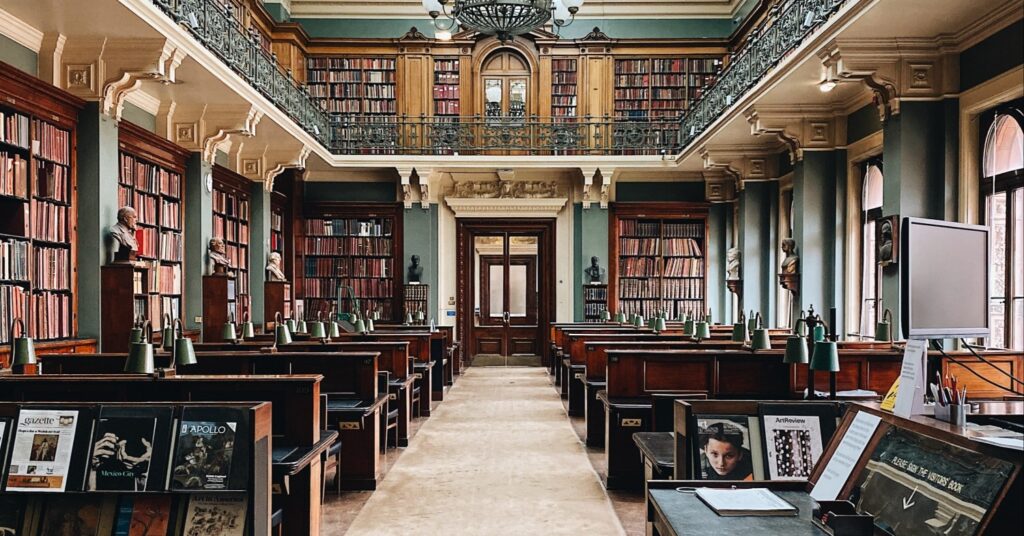 Front look into reading room of an old library, with two floors of shelving and wooden desk cubbies.