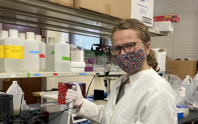 Psychology student, Hailey Beaty, holds up a micro pipet while standing in Dr. Karyn Frick's lab.