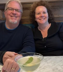 A man and woman sit beside each other at a dinner table, a martini glass in front of them.