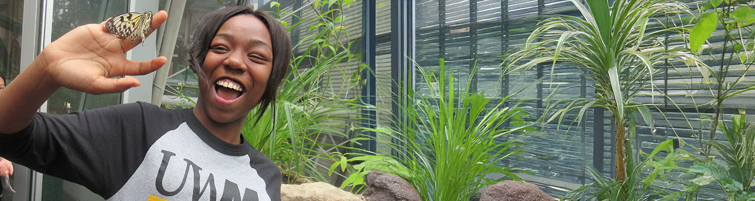 Smiling student in butterfly room with a butterfly on her hand