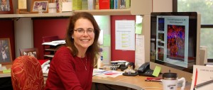 Dr Frick at her desk with a computer screen displaying colorful scientific images