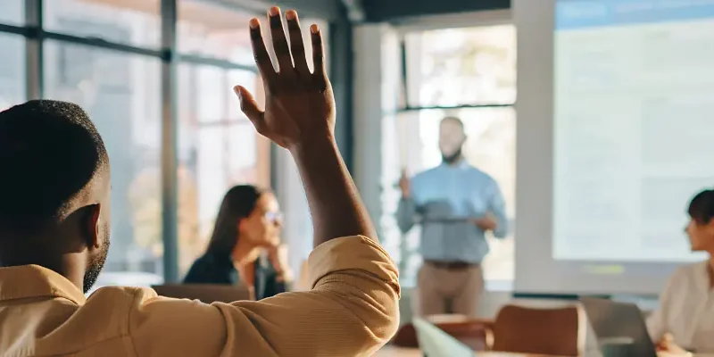 people in a meeting setting; one person's hand is raised