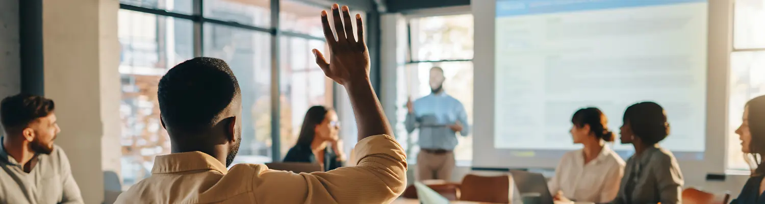 people in a meeting setting; one person's hand is raised