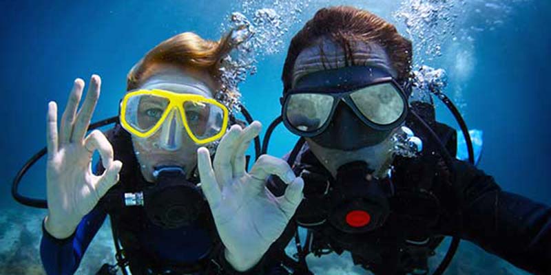 Underwater shot of a young couple diving with scuba in a tropical sea and showing ok signal.
