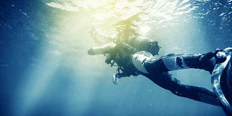 Diver underwater with sunlight breaching surface.