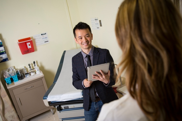 Jake Luo stands with a tablet in a doctor's office talking with a doctor about Center for Health Systems Solutions.