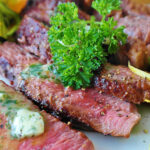 A plate with cuts of cooked beef and a sprig of parsley.