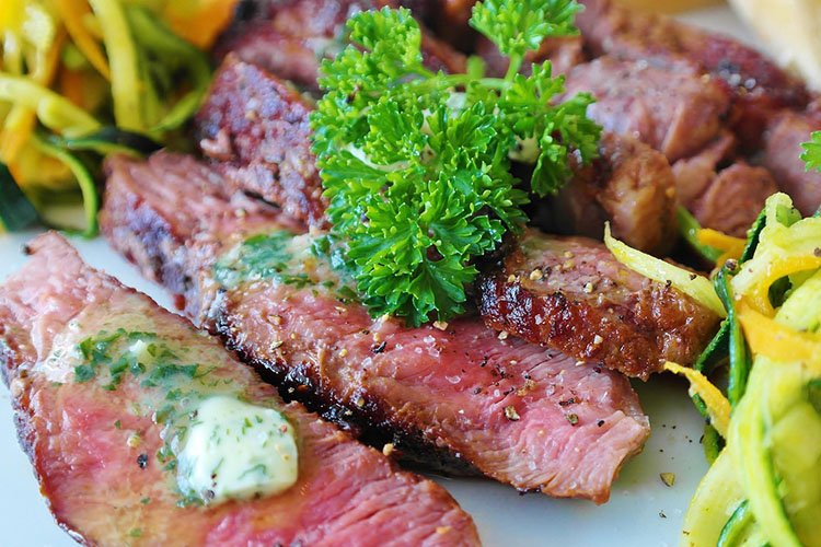 A plate with cuts of cooked beef and a sprig of parsley.