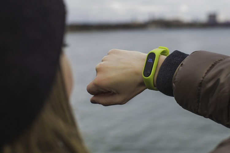 A woman looks at a lime green health tracker on her wrist with a body of water in the background.