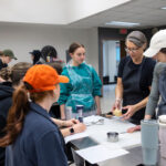 Michelle Rimer instructs a group of UWM students as they stand around a table in the university's teaching kitchen.