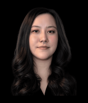 Headshot of Peggy Harsh with long black hair, wearing a black blouse and a septum piercing, against a black background.