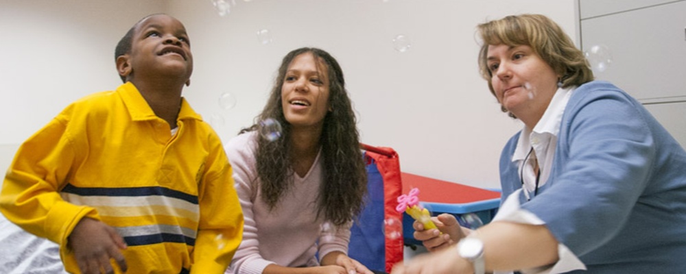 Professor Shelley Lund and Communication Sciences & Disorders student works with a child using augmentative and alternative communication device to describe bubbles.