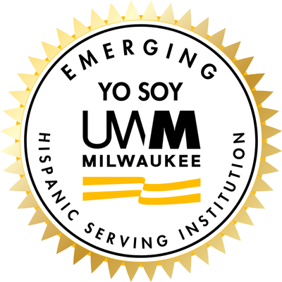 Circular emblem with gold border featuring the text "EMERGING YO SOY UMM MILWAUKEE" and the words "HISPANIC SERVING INSTITUTION" on a white background, with two yellow stripes at the bottom.
