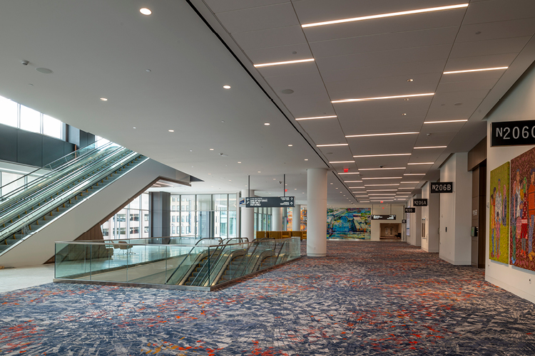 Baird Center escalator and empty hallway with colorful carpeting, fluorescent lights and windows.