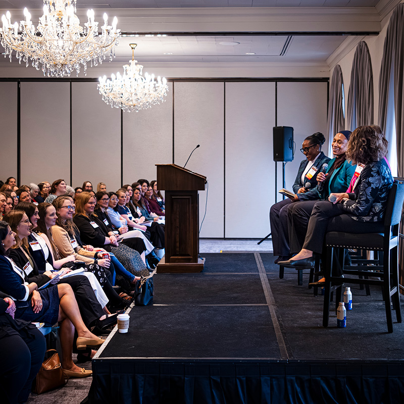 Women Leaders conference breakout speakers sit on stage in front of an audience.