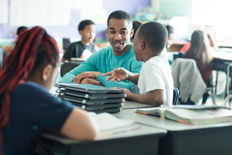Black male student working with school age children in a classroom