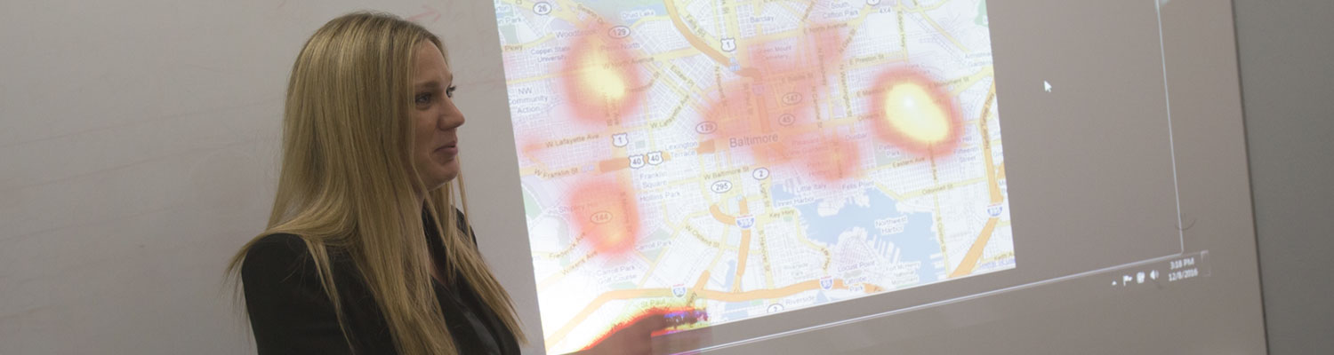 Criminal justice and crime analysis professor (white female) standing in front hotspot map projected onto a wall.