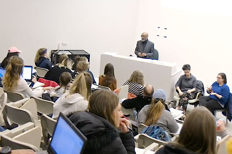 Social Work Associate Professor David J. Pate Jr. (black man) teaches to a packed lecture hall. There are ASL interpreters in the front of the room.