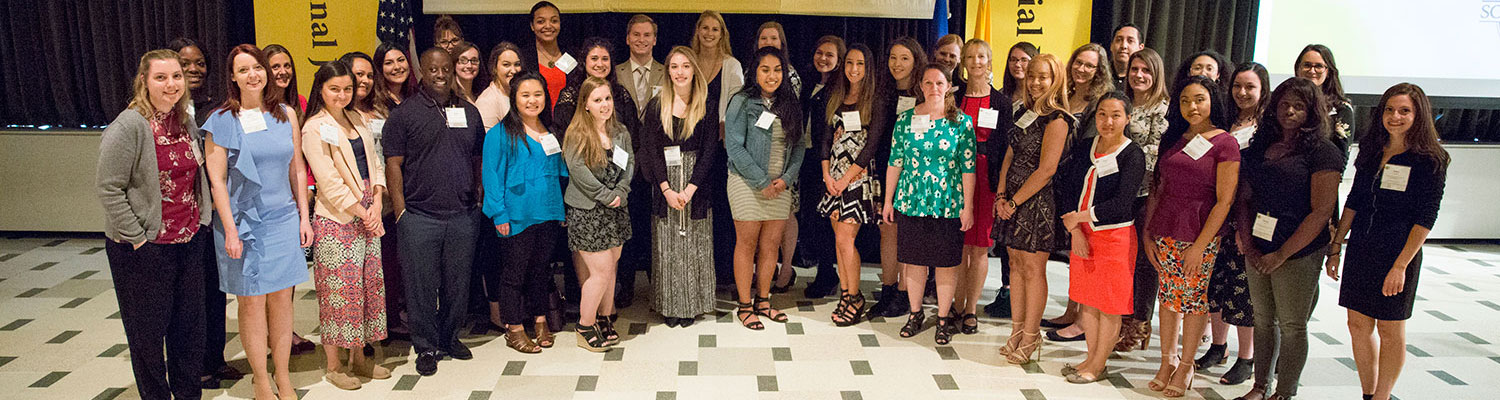 A diverse group of students standing in front of a banner during a scholarship awards ceremony.