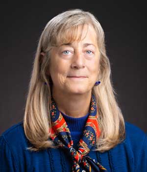 Headshot of professional white woman wearing blue sweater and colorful scarf.