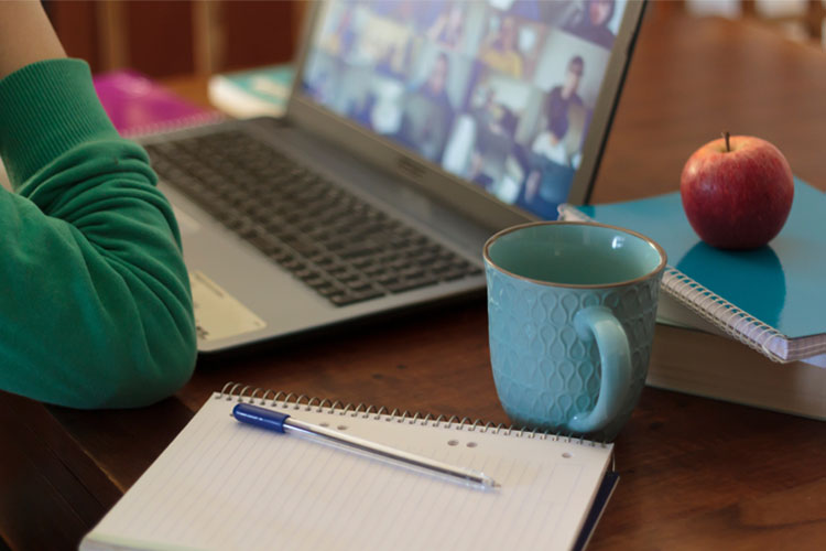 Photo of person at laptop with coffee cup attending online workshop.