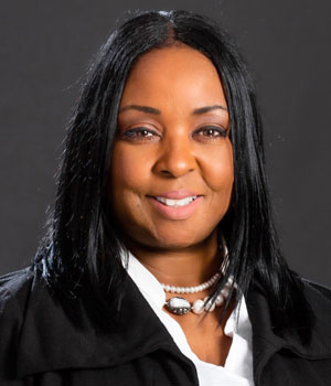 Headshot of Black female professional with white necklace and blazer.