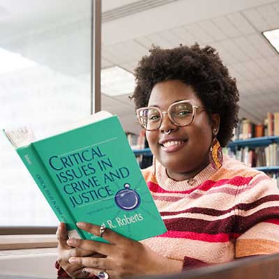 Photo of Helen Bader School of Social Welfare Spring 2023 graduate Amillia Heredia (african american woman) holding a book