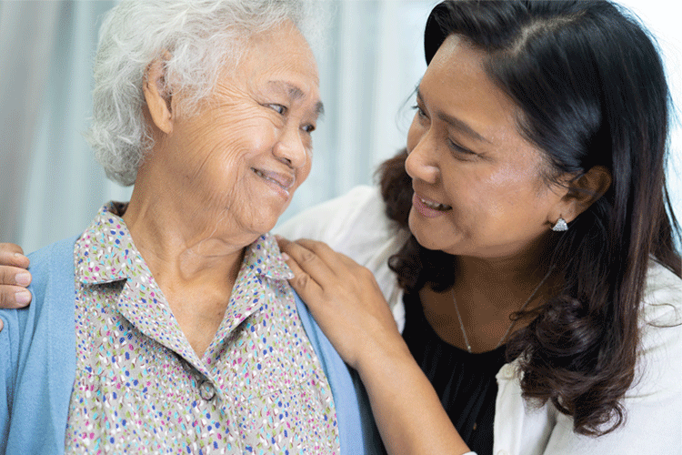 Older Asian female interacting and smiling with Asian female caregiver in a clinical setting.