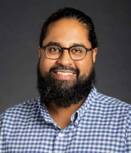 Professional headshot of East Indian male in checkered blue shirt.