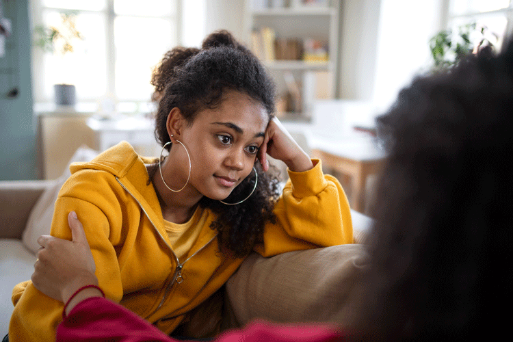 Black teen engaging with parent and chatting on the couch in a warm, home setting.