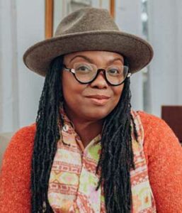 Environmental headshot of creative professional (Black female) wearing hat and colorful patterned scarf.