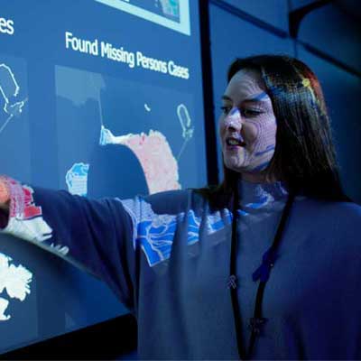 Crime Analyst (white female) pointing out details of crime map that's projected onto the wall in a dark room.