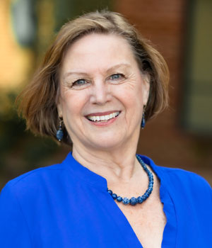 Outdoor professional headshot of white female with cropped light brown hair wearing a blue necklace and blue blouse.