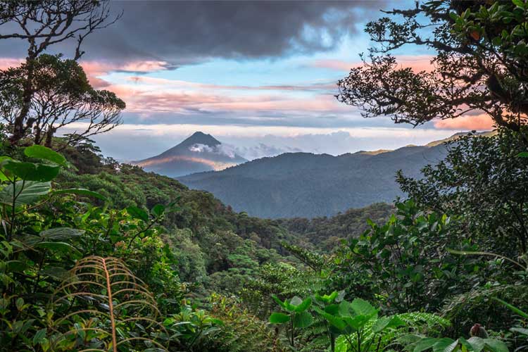 Lush foreground with sloping hills in the distance frames a volcano in Cosa Rica.