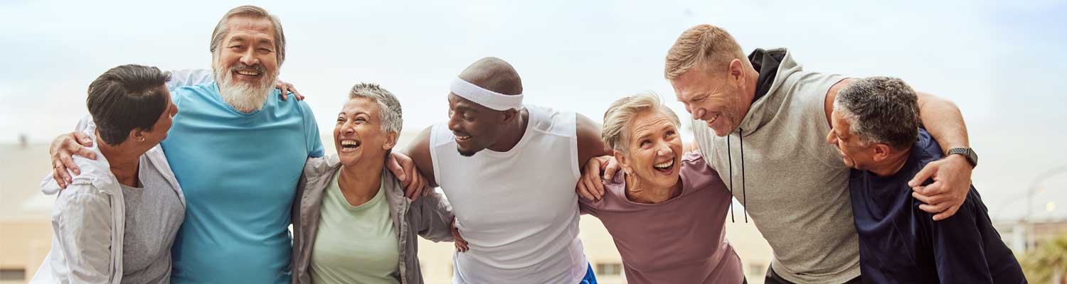 Group of diverse older adults in active clothing huddled together outside enjoying one another's company.