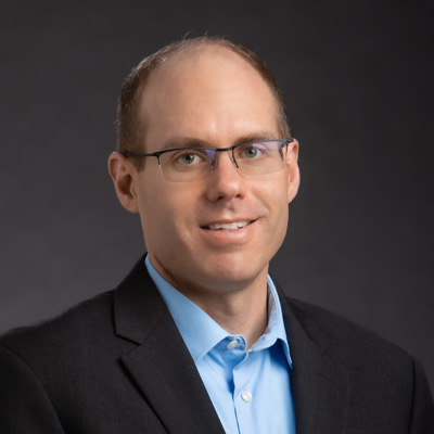Professional headshot of white male with glasses, blue shirt and black blazer.