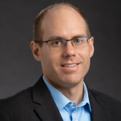 Professional headshot of white male with glasses, blue shirt and black blazer.
