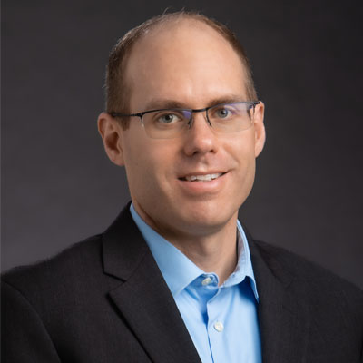 Professional headshot of white male with glasses, blue shirt and black blazer.