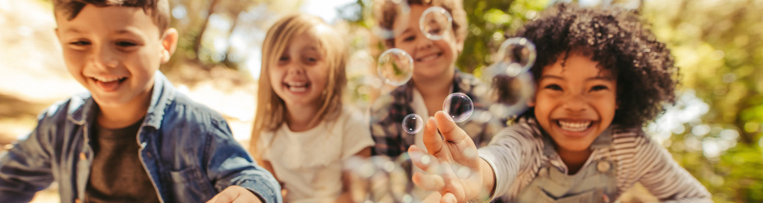Diverse children smiling and playing with bubbles.