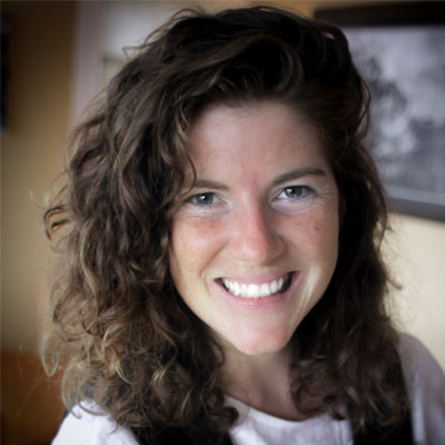 Headshot of smiling film producer (white woman) in a well-lit room with a black and white photo on the wall in the background.