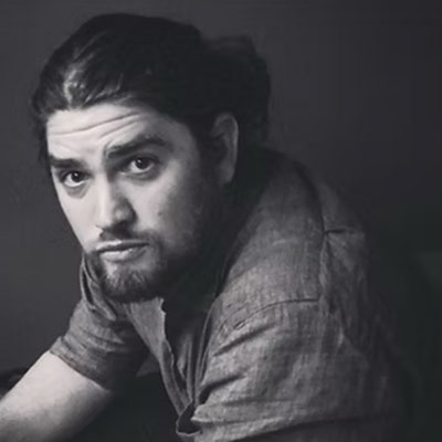 Black and white artistic headshot of cinematographer (white male) with a pony tail and beard.