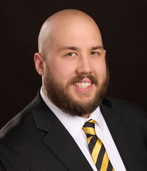 Professional headshot of multi-ethnic male wearing black suit and striped tie.