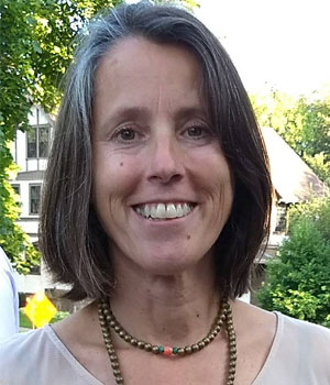 Headshot of white woman standing outside with green trees in the background.