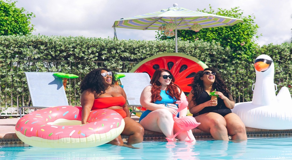 three women sitting poolside with three pool inflatables surrounding them