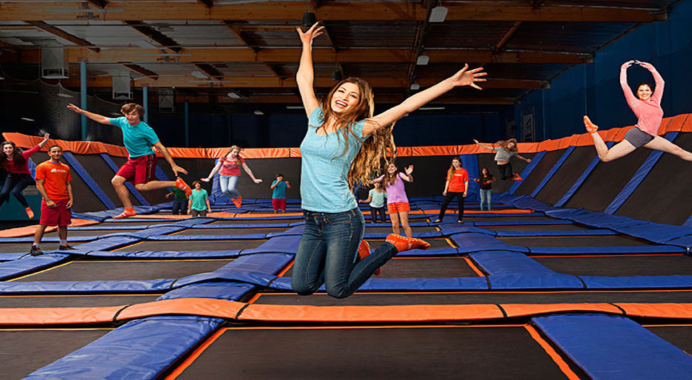 Woman jumping on a trampoline at a trampoline park. There are children in the background also jumping on trampolines.