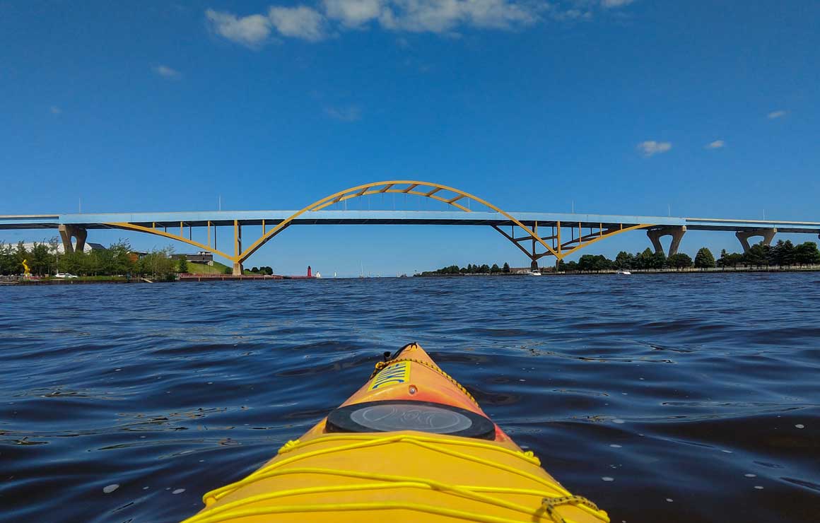 Photo of a kayak sailing on lake Michigan. The Hoan Bridge is visible on the horizon.